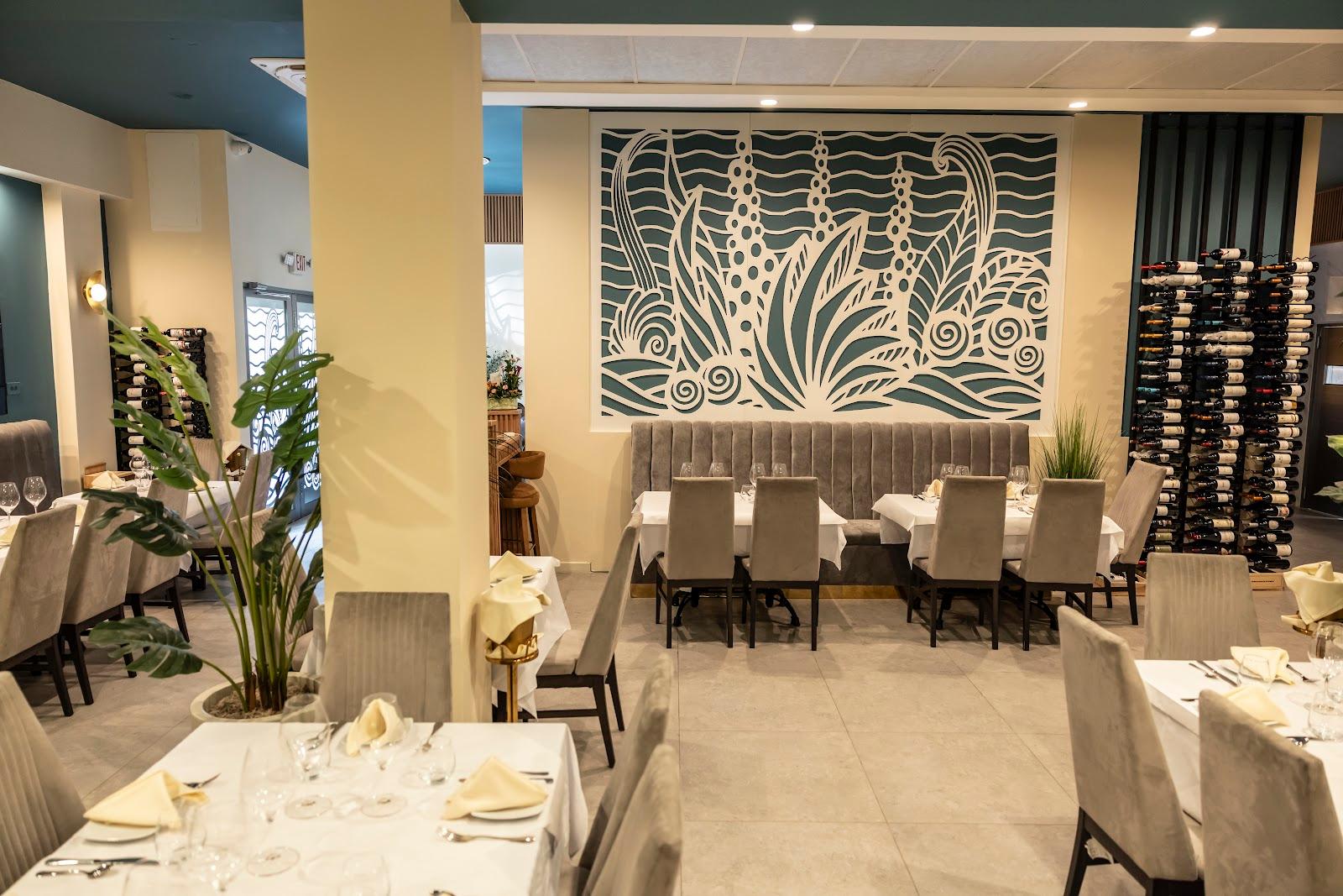 Interior de restaurante con mesas elegantes, mural tropical en tonos verde y crema, y vinoteca al fondo.