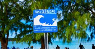 Bañistas frente a una señal de alerta de zona de tsunami escrita en español en una playa de Puerto Rico.